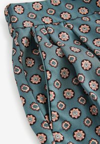 Geheel met een teal achtergrond met florale motieven in koper, blauw en wit. Gelaagd met subtiele strepen en gedrapeerde plooien.