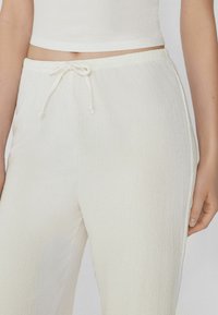 Pantaloni bianchi, leggeri e texture, con vita elastica e dettaglio con coulisse, caratterizzati da una vestibilità comoda e rilassata.