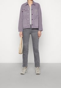 Lichtpaarse spijkerjack met voorzakken, grijze jeans, glanzende beige handtas en grijze sneakers met textuurelementen, tentoongesteld op een neutrale achtergrond.