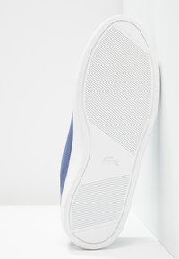 Sneaker en tissu texturé bleu marine avec une semelle en caoutchouc blanc, présentant des rainures horizontales et un petit logo près du talon.