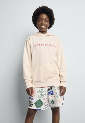Beige hette med rosa "JORDAN" tekst, kengurulomme. Kombinert med hvite shorts med flerfargede logoer og mønstre.