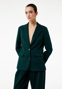 Donkergroene blazer van maatwerkstof, met een gekleed kraag, twee voorkeurszakken en knoopsluiting. Glad oppervlak, moderne pasvorm.