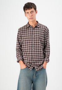 Brown plaid shirt with light blue accents, button-up front, and rolled sleeves, paired with loose blue denim shorts.