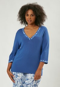 Top blu in maglia con scollo a V, maniche a tre quarti e accenti a fantasia in blu chiaro. Texture morbida, design casual.