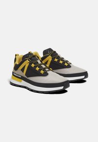 Lichtgrijze en zwarte sportschoenen met gele accenten, textiel bovenmateriaal, dikke witte tussenzool en contrasterende zwarte rubberen outsole.