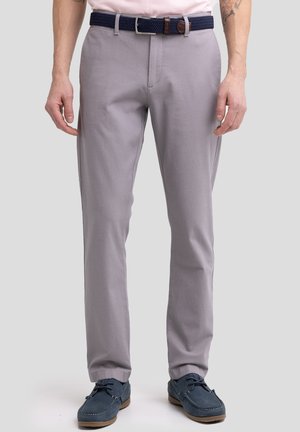 Pantalones ajustados en gris claro, confeccionados en una mezcla de algodón. Presentan un cinturón tejido en color marino y se combinan con zapatos marinos.