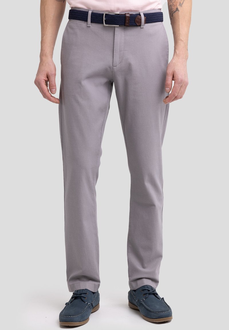 Pantalones ajustados en gris claro, confeccionados en una mezcla de algodón. Presentan un cinturón tejido en color marino y se combinan con zapatos marinos.