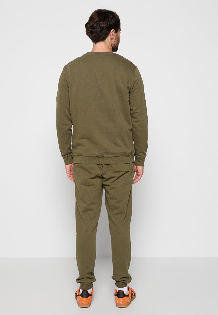 Ensemble de sweat-shirt et pantalon de jogging vert olive. Tissu doux, poignets et taille côtelés. Baskets avec des accents noirs et oranges. Design minimaliste.