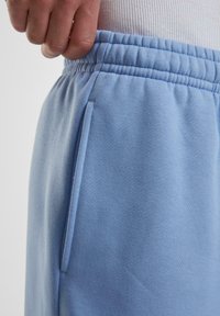 Lyseblå sweatpants lavet af blødt stof, med en afslappet pasform, elastisk talje og en sidelomme.