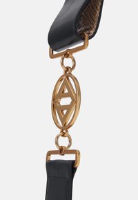 Bracelet en cuir noir avec un intérieur texturé, dotée d'un matériel en or en forme d'oval avec un design géométrique en relief, relié par un anneau en or.