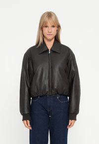 Veste bomber en cuir noir avec un grand col, fermeture éclair et poignets côtelés. Légère et ajustée avec un ourlet arrondi.