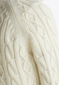 Gros plan sur un tissu tricoté de couleur crème avec des motifs complexes de torsades et de losanges, en texture douce de fil.