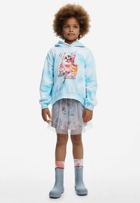 Sininen, liukuvärjätty huppari, jossa kissakuva, kerrospukeutuneena läpikuultavan eläinaiheisen hameen kanssa. Yhdistetty sinisiin saappaisiin ja vaaleanpunaista korostavia sukkiin.