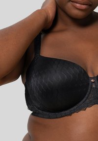 Zwarte bh met kantafwerking en gladde voorgevormde cups, voorzien van een textuurpatroon, verstelbare schouderbanden en een decoratief accent aan de voorkant.