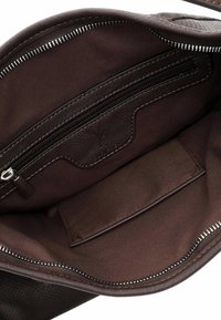 Intérieur d'un sac en cuir marron présentant une doublure en tissu lisse, une poche zippée et un logo en relief sur un panneau marron.