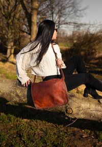 Borsa a spalla in pelle marrone con una texture liscia e forma arrotondata, dotata di una lunga tracolla e pochi dettagli in metallo.