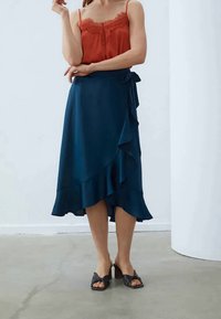 Navy wrap skirt with ruffled hems, made of smooth fabric. Paired with a red lace-trimmed camisole and black heeled sandals.