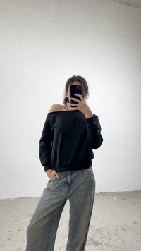 Fekete, off-shoulder pulóver hosszú ujjal, világosszürke, bő szárú farmernadrággal párosítva. Simább textúra és laza szabás.