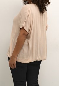 Lichtbeige, gewatteerde top met korte mouwen, ontspannen pasvorm en een afgeronde zoom, gecombineerd met zwarte slim-fit broeken.