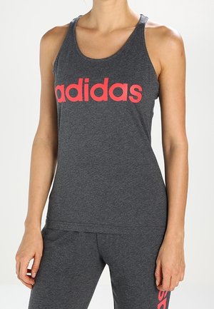 Kobieta ubrana w ciemnoszary bezrękawnik Adidas i dopasowane spodnie z czerwonym napisem logo Adidas na obu.