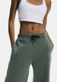 Lightweight, olive green joggers made of soft fabric, featuring an elastic waistband with a black drawstring and side pockets.