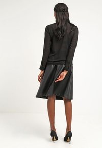 Svart genomskinlig blus med långa ärmar, matchad med en svart faux läderkjol. Högklackade skor fulländar outfiten; släta texturer och enkel design.