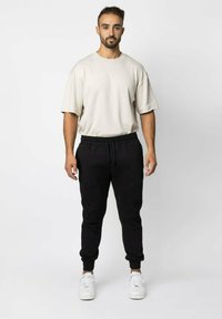 Crème oversized t-shirt en zwarte joggings gemaakt van zachte stof. De joggers hebben een elastische tailleband en zijn aan de onderkant afgewerkt met een boordje. Witte sneakers maken de uitstraling compleet.