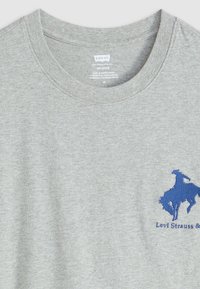 Grijze katoenen t-shirt met een ronde hals en een blauwe geborduurde cowboyafbeelding op de linker borst met daaronder de merknaam.