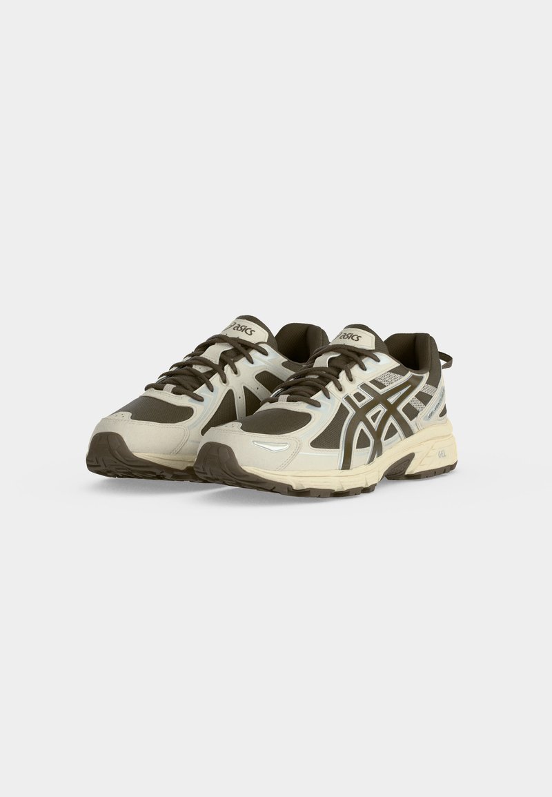 Par de zapatillas de correr ASICS en beige y marrón oscuro con diseño de cordones y suelas de goma texturizadas, mostradas sobre un fondo claro y liso.