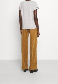 Grå kortärmad t-shirt med "POLO"-logotyp på ärmen, ihop med hög midja och vida byxor i senapsgul kordflors med en texturerad yta.