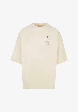 Short-sleeve, cream-colored t-shirt made of soft cotton. Features a small black hand graphic with a red heart on the left chest.