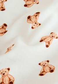 White fabric with a repeating pattern of small, light brown teddy bears, showcasing soft textures and a playful design.