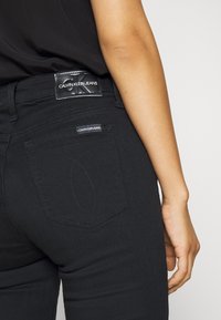 Mustat farkut slim fit -mallilla, joissa on nahkainen vyötärömerkki, erottuva ompelu ja kaksi taustataskua räätälöidyllä muodolla.