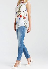 Chemisier blanc sans manches avec imprimé floral et pois, associé à un jean skinny bleu clair et des chaussures blanches à talons hauts avec lanières.