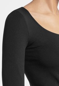 Svart långärmad åtsittande topp tillverkad av ett mjukt stretchtyg. Har en vid rund halsringning och minimala sömmar för en ren look.