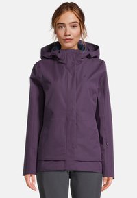 Donna che indossa una giacca impermeabile viola con cappuccio, tasche frontali e bottoni Automatici, in piedi su uno sfondo neutro.