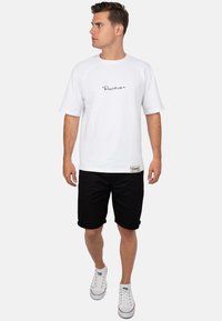 T-shirt en coton blanc à manches raglan courtes et un logo en cursive noir. Associé à un short noir jusqu'aux genoux et des baskets blanches.