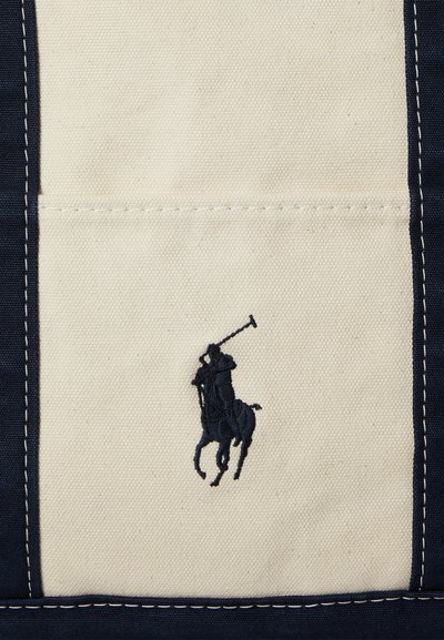 Jucător de polo negru brodat cu malet pe un panou de țesătură crem, încadrat de o țesătură bleumarin cu cusături albe.