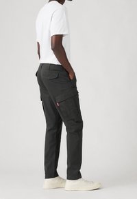 Schwarze Cargo-Hosen mit Seitentaschen, taillierter Schnitt und robustem Material. Kombiniert mit einem weißen T-Shirt und weißen Sneakern.