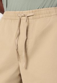 Beige shorts med elastisk talje og snor, med en glat stofoverflade og minimal syning.