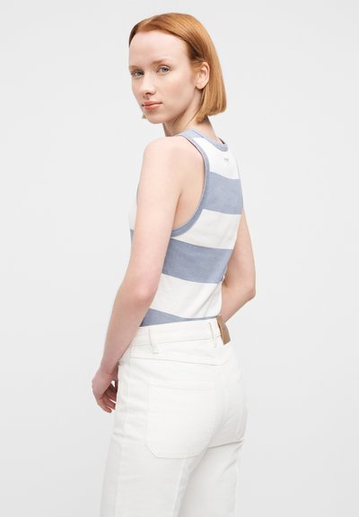 Αμάνικο τοπ σε λευκό με οριζόντιες μπλε ρίγες· διαθέτει στρογγυλή λαιμόκοψη και εφαρμοστή σιλουέτα, συνδυασμένο με λευκό παντελόνι ψηλόμεσο.