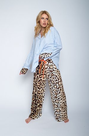 Gestreept blauw oversized shirt met lange mouwen, gecombineerd met losse broek met luipaardprint en een oranje trekkoord. Zachte stoftextuur.