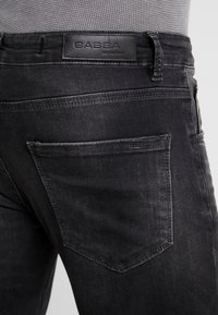 Vaqueros de denim negros con una textura suave, de corte ajustado, que cuentan con un bolsillo trasero y una etiqueta de cuero con marca en la cinturilla.