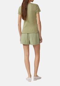 Olijfgroene ribbeltrui met korte mouwen en gekartelde randen, gecombineerd met bijpassende losse shorts en witte mesh instappers.