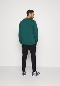 Sweatshirt teal à col rond et manches longues, associé à un jogging noir. Les accessoires incluent des baskets avec des accents blancs.