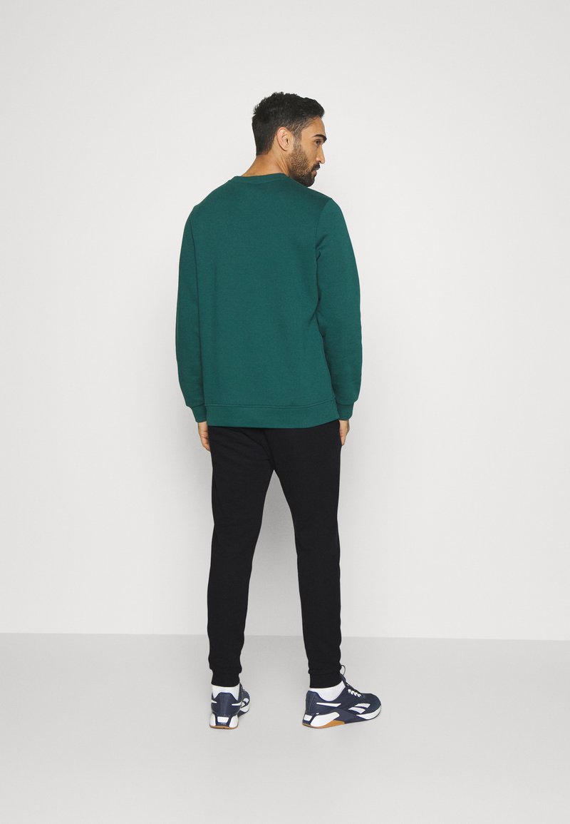 Turkusowa bluza z okrągłym dekoltem i długimi rękawami, zestawiona z czarnymi dresami. Dodatki to sneakersy z białymi akcentami.