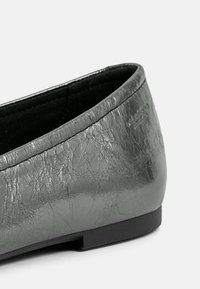 Platte schoen van gestructureerd grijs synthetisch materiaal, met een gladde afwerking en een lage zwarte rubberen zool. Rond de teen met subtiele stiksel detail.