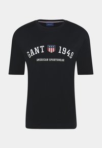 Marineblå bomulds t-shirt med rund halsudsk�æring, korte ærmer og hvid tekst med et skjoldemblem, der viser røde, hvide og blå accenter.