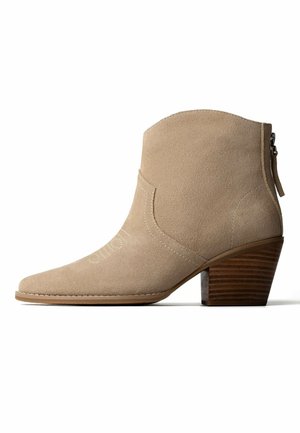 Beiger Wildleder-Knöchelstiefel mit gestapeltem Blockabsatz aus Holz, seitlichem Reißverschluss und Ziernähten am Obermaterial und an der Spitze.