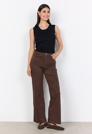 Black ribbed tank top with scalloped trim, brown wide-leg pants, and dark slip-on shoes with gold accents. Model stands against a white background.